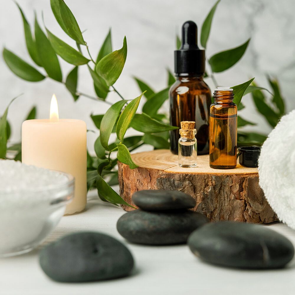 beauty treatment items for spa procedures on white wooden table with green plant. massage stones, essential oils and sea salt with burning candle